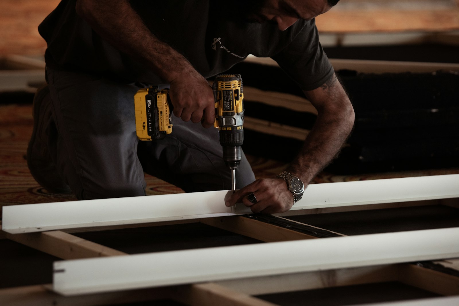Worker using a cordless drill to fasten white boards on a wood frame