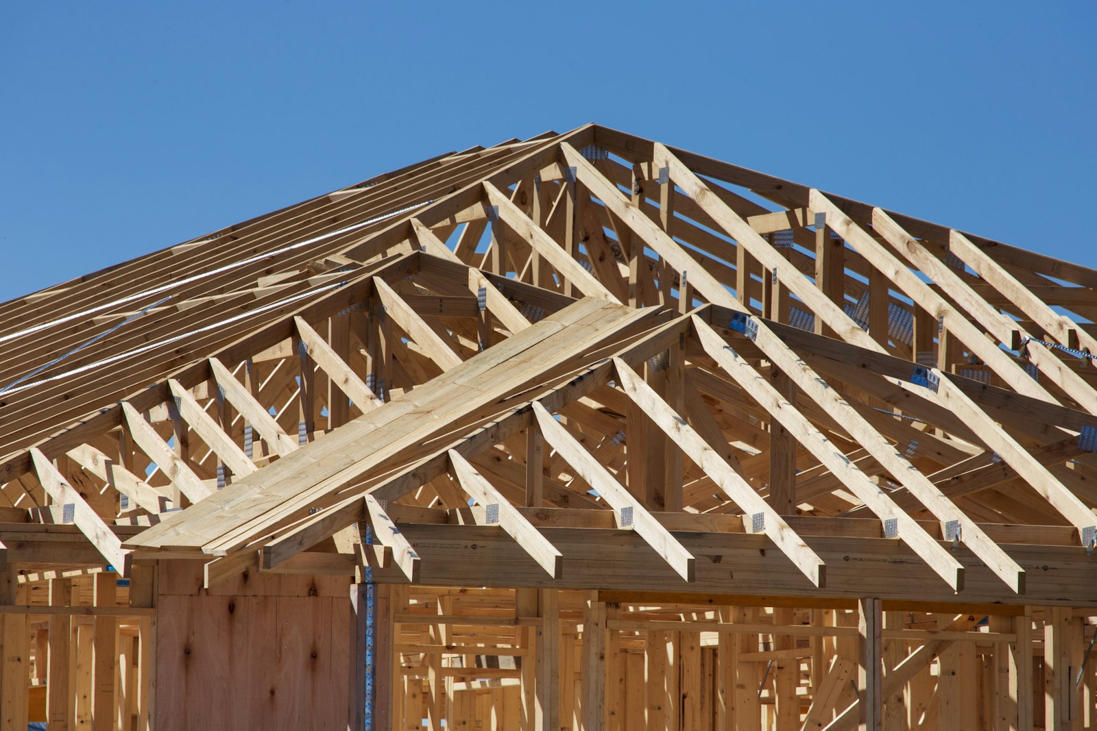 Wood roof trusses and wall framing on a house under construction against a blue sky