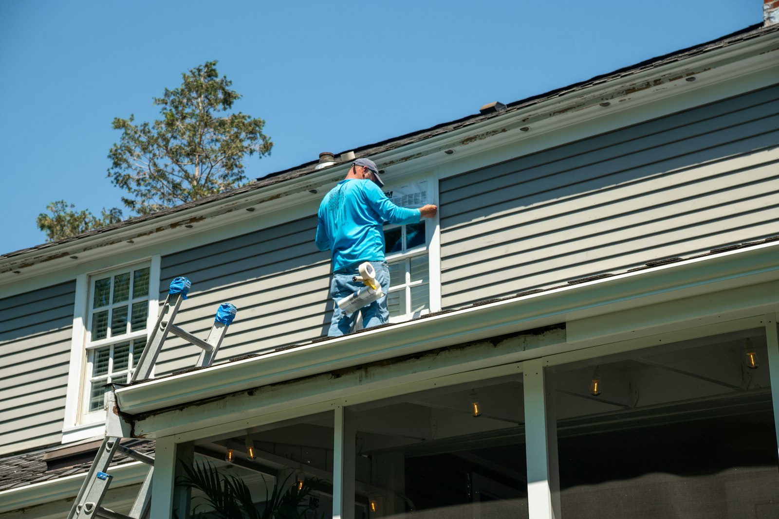 Worker on a ladder doing exterior work on the upper story of a gray-sided house