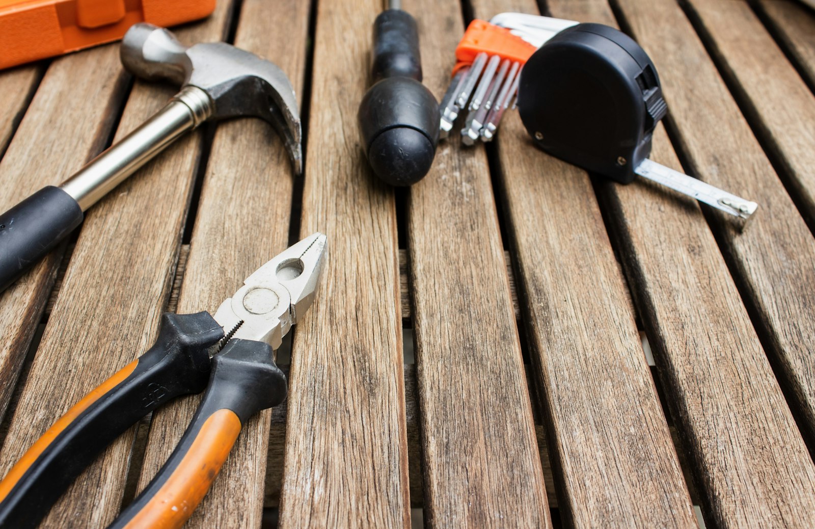Hammer, pliers, screwdriver, hex keys and a tape measure laid out on a wooden deck