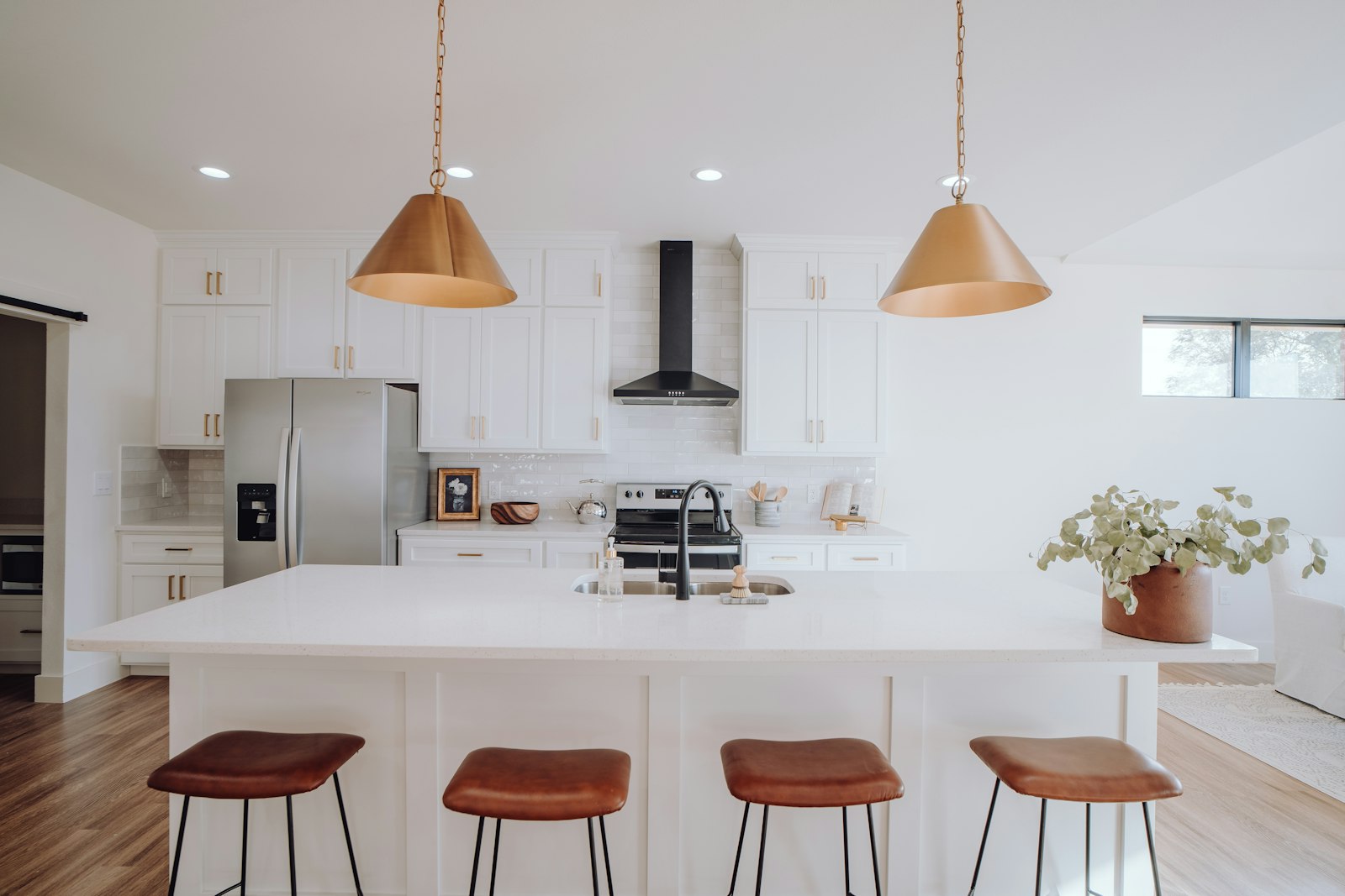 White kitchen with a large island, wood bar stools and copper pendant lights